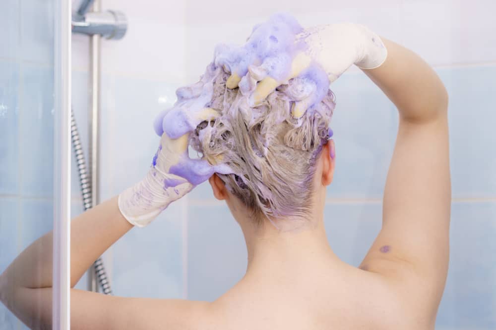 Purple toner shampoo being used in the shower by a blonde woman